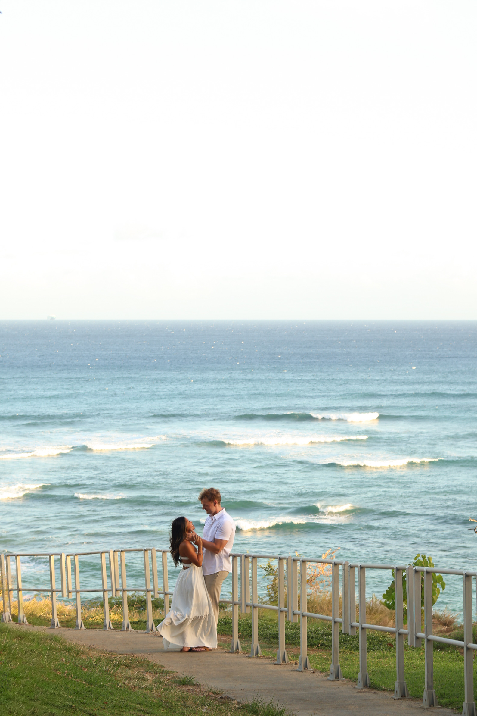 Couple at wooden railing with serene ocean view and palm trees